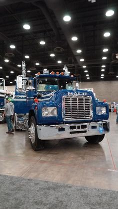 a large blue truck parked inside of a warehouse next to other trucks and people standing around