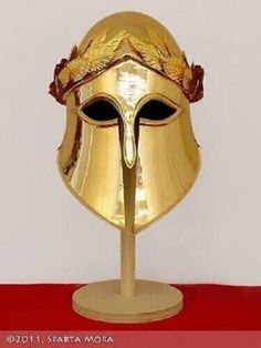 a golden helmet on a stand with a red table cloth behind it and a white wall in the background