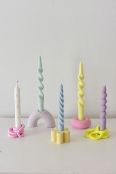 there are many candles that are on the table and one is pink, blue, green, yellow