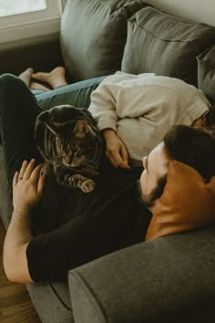 a man laying on top of a couch next to a woman holding a cat in his lap
