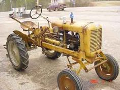 an old yellow tractor parked in a parking lot
