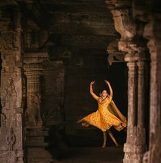 a woman in a yellow dress is dancing inside an ancient building with columns and pillars
