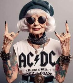 an older woman with white hair and tattoos holding her hands up in the air while wearing sunglasses