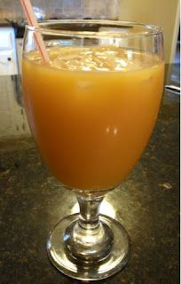an orange drink in a glass with a straw on the top and another beverage behind it