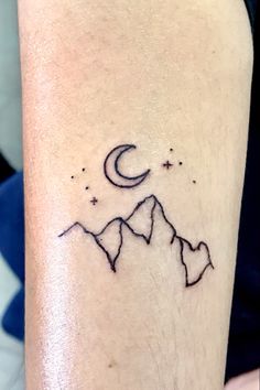 a small tattoo on the leg of a woman with mountains and stars in the sky