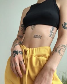 a woman with tattoos on her arm wearing yellow sweatpants and a black crop top
