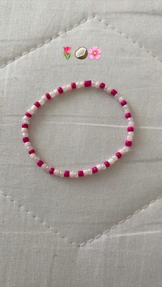 a pink and white beaded bracelet sitting on top of a piece of cloth next to a button