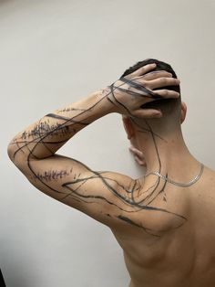 a man with his hands on his head has tattoos on his body and is looking at the mirror