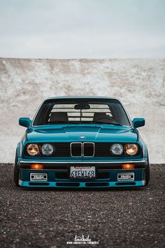 a blue bmw is parked in front of a white wall with snow on the ground
