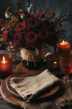 a table topped with candles and flowers next to a vase filled with red roses on top of a wooden plate