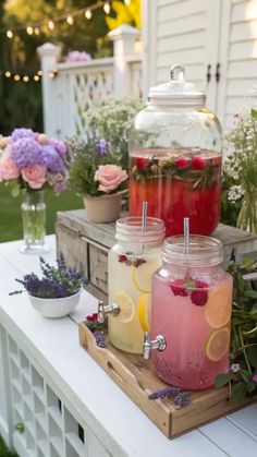 three jars filled with drinks sitting on top of a table next to flowers and potted plants