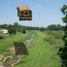 a school bus is flying over a stream in the middle of a grassy field with trees