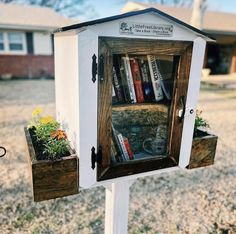 a wooden book shelf with books in it on top of a white post next to a yard