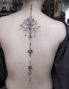the back of a woman's neck with an intricate tattoo design on her lower back