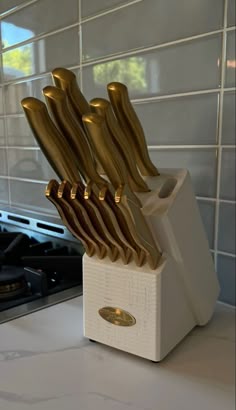 gold knives are stacked in a white holder on the counter top next to a stove