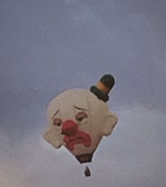 a clown balloon flying in the sky with a hat on it's head and nose