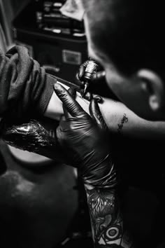 a man getting his arm tattoo done by another person with black gloves and tattoos on