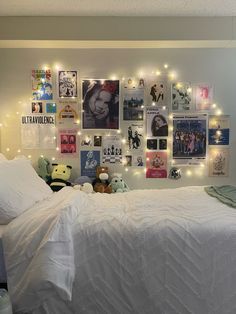 a bed with white sheets and lights on the wall above it is decorated with pictures