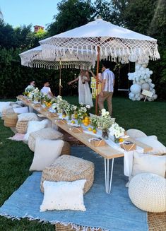 an outdoor table set up for a party with white pillows and flowers on the ground