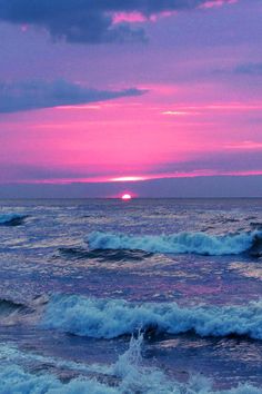 the sun is setting over the ocean with waves crashing in front of it and pink clouds