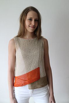 a woman standing in front of a white wall with an orange and beige sweater on