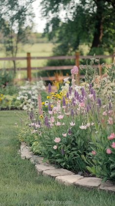 a garden filled with lots of flowers next to a lush green field and wooden fence
