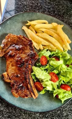 a plate with meat, fries and lettuce on it next to a salad