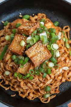tofu and noodles in a wok with sesame seeds, scallions and green onions