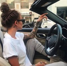 a woman sitting in the driver's seat of a car with tattoos on her arm