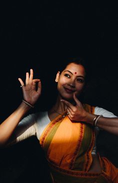 a woman in an orange and yellow sari making the vulcan sign with her hands