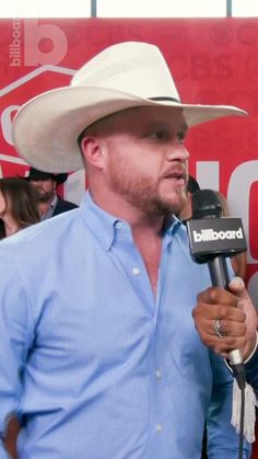 a man wearing a cowboy hat and holding a microphone in front of a red sign