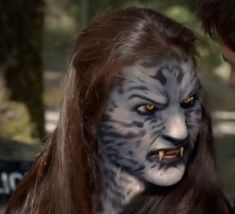 a woman with white and black face paint next to a man wearing long brown hair