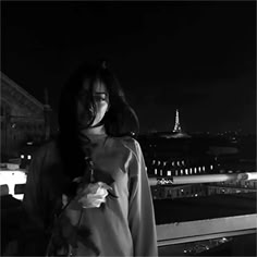 a woman standing on top of a roof next to a building at night with her hand in her pocket