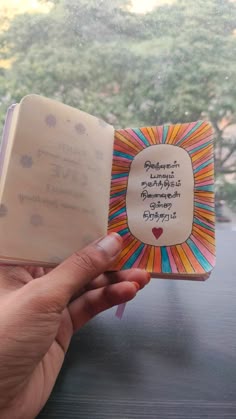 a person holding an open book in front of a window with trees and sky outside