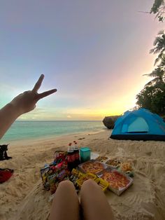 the person is sitting on the beach with their feet in the sand and pointing to the sky