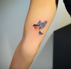 a small blue bird tattoo on the left inner arm and wrist, with an orange breast