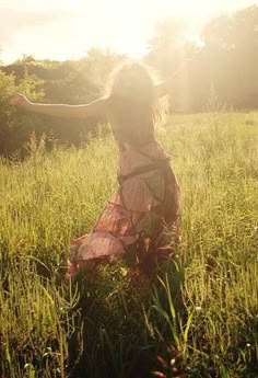 a woman is walking through the grass with her arms spread out to catch something in the air