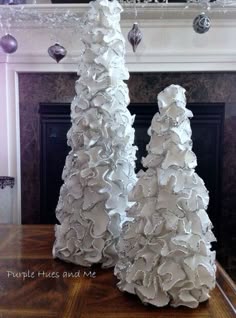 two white christmas trees sitting on top of a wooden table in front of a fireplace