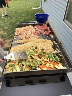 an outdoor bbq grill with vegetables and meats being cooked on it's side