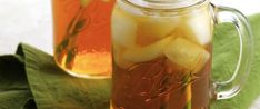 two mason jars filled with iced tea on top of a green cloth next to leaves