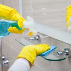 two hands in yellow gloves are cleaning a mirror with soap and detergent on it
