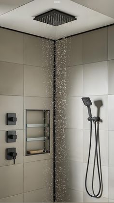Modern ceiling-mounted rain shower head system in a spa bathroom with waterfall streams, tile walls, and glass enclosure