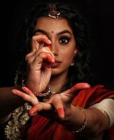 a woman in a red and white sari holding her hands up to her face