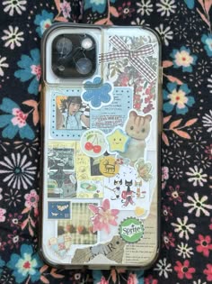 an iphone case with stickers on it sitting on a flowery surface, next to a phone charger