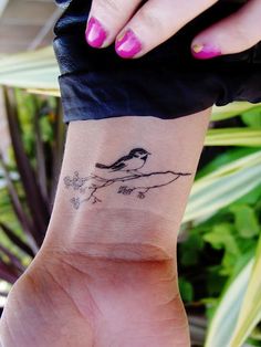a woman's wrist with a small bird on top of the tree branch tattoo