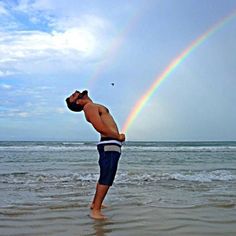 a man standing in the ocean with a rainbow behind him