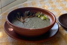 a brown bowl filled with green soup on top of a wooden table next to a plate