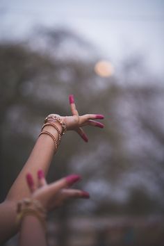 two hands with pink manicures and rings on their fingers, reaching for the sky