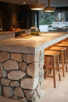 a kitchen island made out of rocks with stools around it and lights hanging from the ceiling