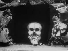 the skeleton is standing in front of an entrance to a cave with two men on it